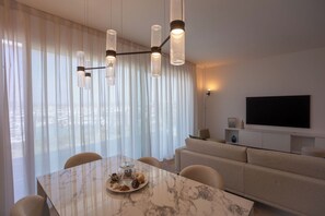Ein modernes Wohnzimmer mit einem Esstisch aus Marmor, einer Couch und einem an der Wand befestigten Fernseher.