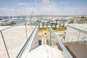 Ein Yachthafen mit zahlreichen vertäuten Booten, einem wolkenlosen Himmel und einem modernen Gebäude mit Glasgeländer und einer Treppe, die nach unten führt.