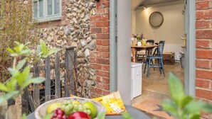 A stone wall with a window, a dining area with a table and chairs, and a bowl of fruit on a table.