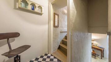 A narrow hallway with a checkered floor, a wooden bench, a shelf with decorative items, and a staircase leading to another room.