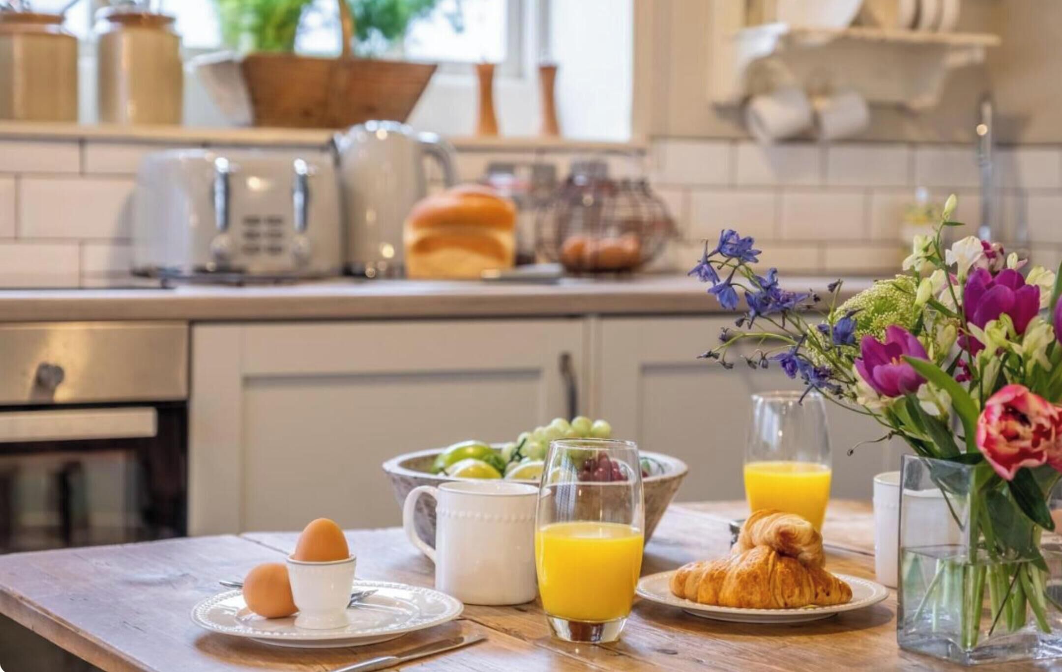 Um café da manhã com ovos, suco, croissants e uma saladeira de frutas.