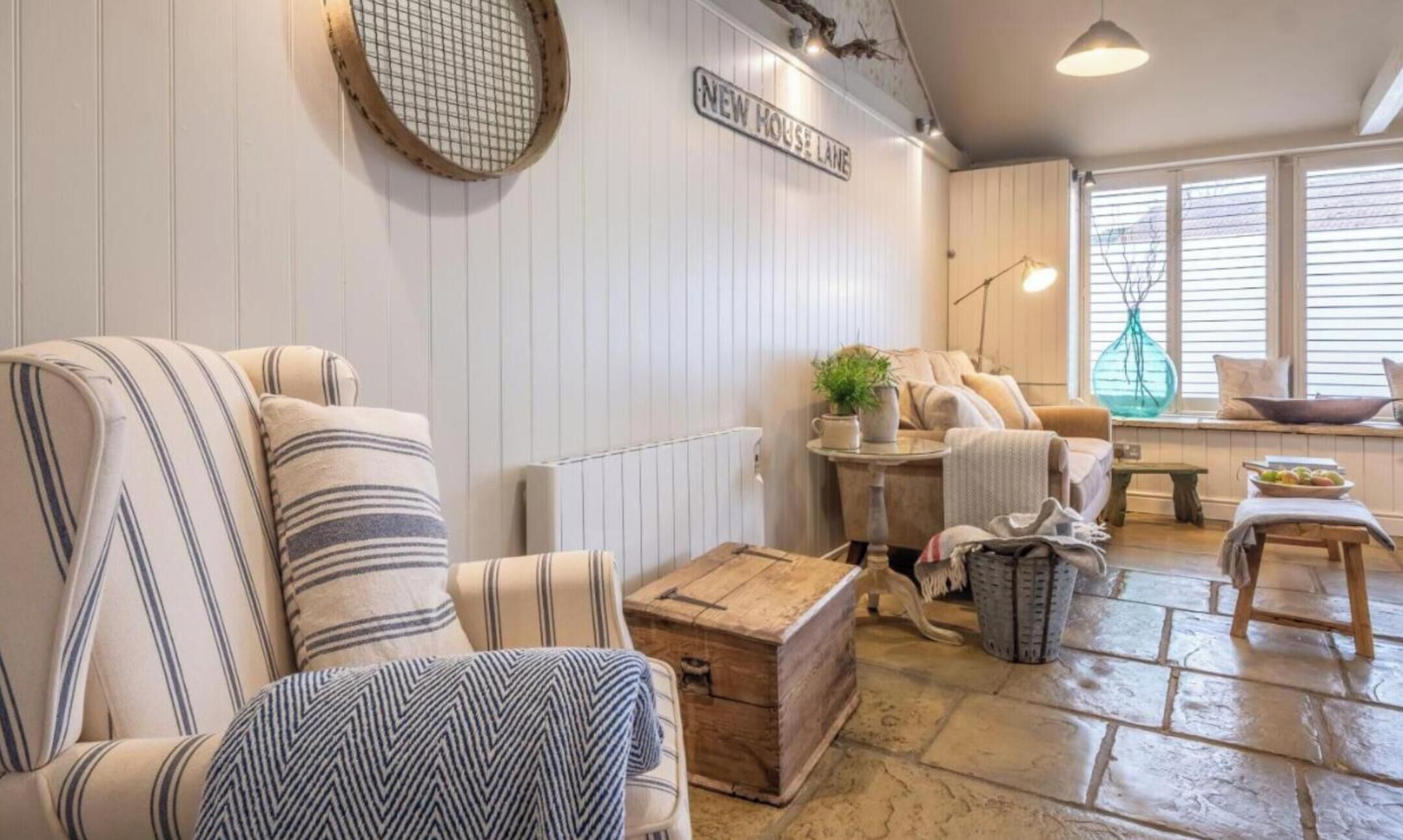 Un salon chaleureux avec des canapés à rayures, une commode en bois et une fenêtre équipée de stores.