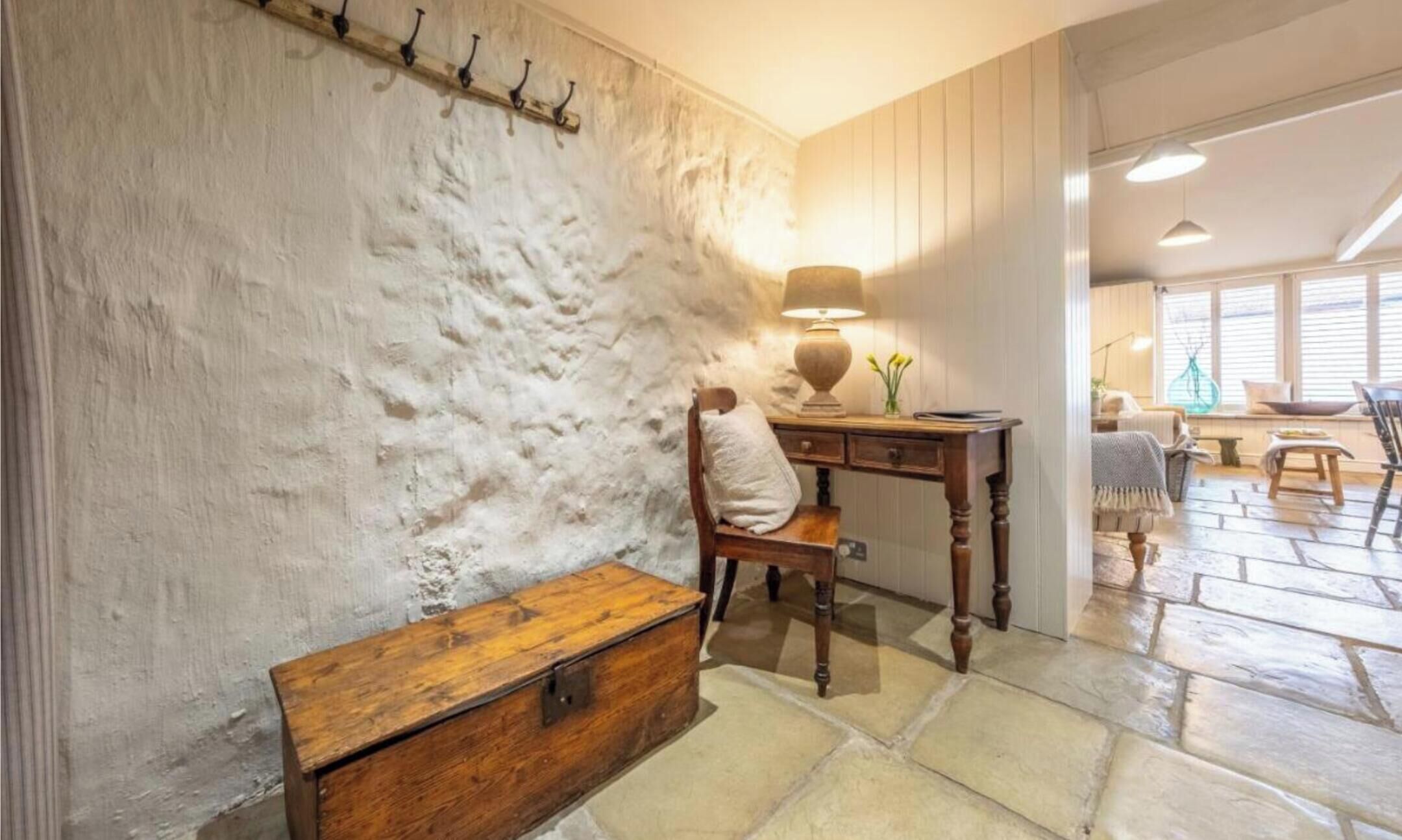 A room with a stone floor, a wooden desk, a chair, a wooden chest, and a lamp.