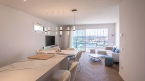 Ein modernes Wohnzimmer mit einer Couch, einer Essecke mit Tisch und Stühlen und Blick auf eine Marina durch große Fenster.
