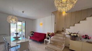 Un salon moderne avec une table à manger en verre, un canapé rouge, un escalier et un coin repas avec des chaises.