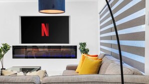 Een moderne woonkamer met een flatscreen televisie aan de muur, een bank met kussens, en een potplant.
