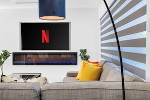 Ein modernes Wohnzimmer mit einem an der Wand befestigten Flachbildfernseher, einer Couch mit Kissen und einer Topfpflanze.