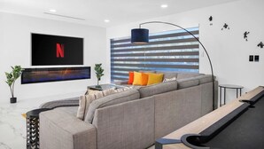 Een moderne woonkamer met een modulaire bank, een wandgemonteerde televisie, een vloerlamp en een gestreepte wand.
