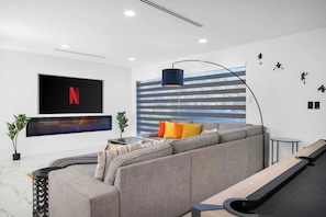 Ein modernes Wohnzimmer mit Ecksofa, Wandfernseher, Stehlampe und einer gestreiften Wand.
