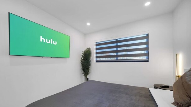 Een moderne hotelkamer met een groot bed, een televisiescherm, een raam met zonwering en een klein tafeltje met een afstandsbediening.