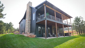A modern two-story house with a stone chimney, a balcony with outdoor furniture, and a well-maintained lawn.