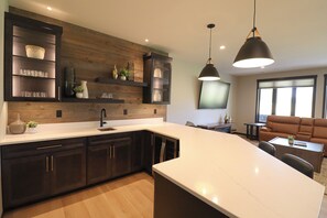 Une cuisine moderne avec des meubles de couleur sombre, un plan de travail blanc et des luminaires suspendus.