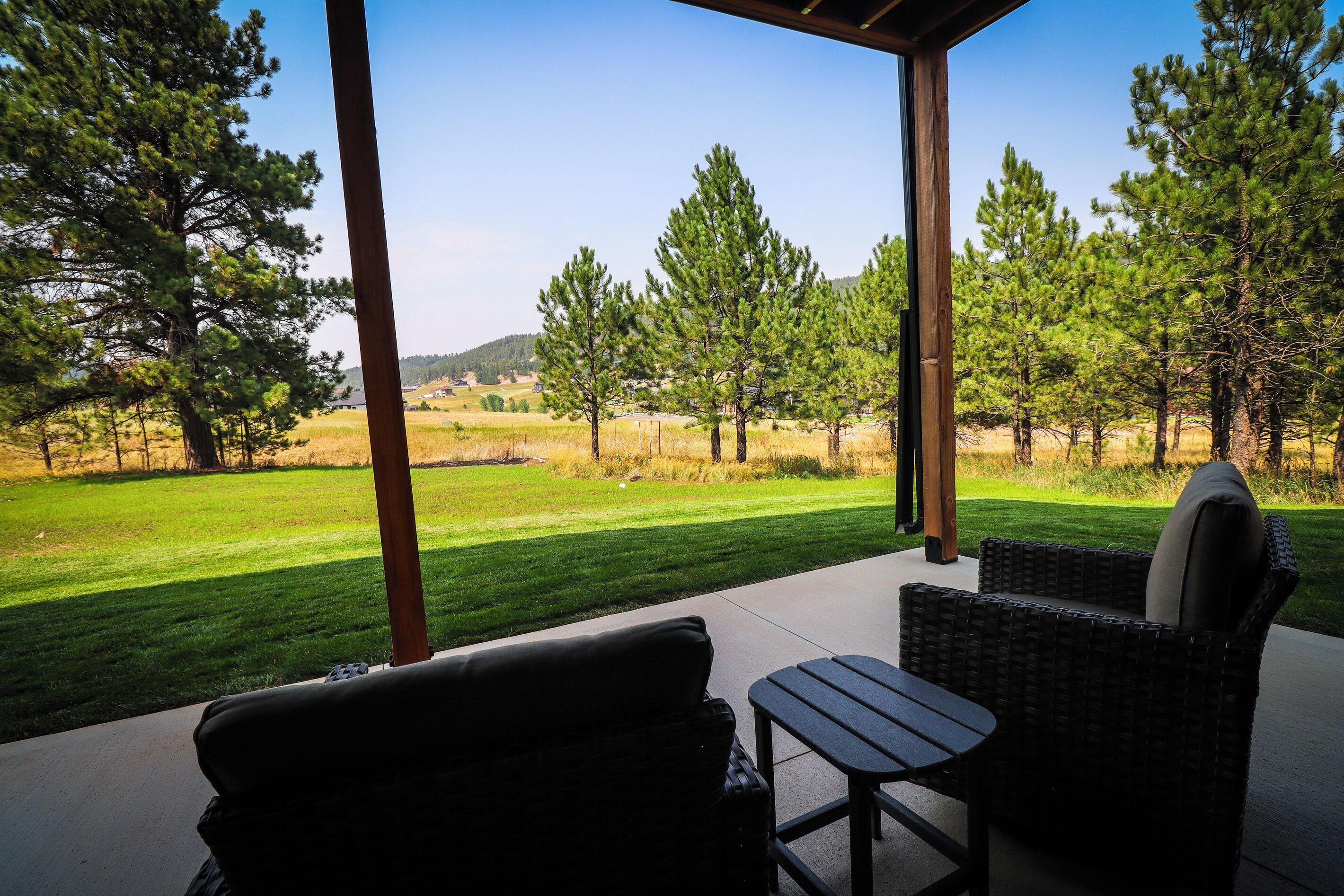 A covered outdoor seating area with a view of a grassy field and trees.