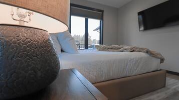 A modern bedroom with a large bed, a bedside table with a textured lamp, and a TV mounted on the wall.