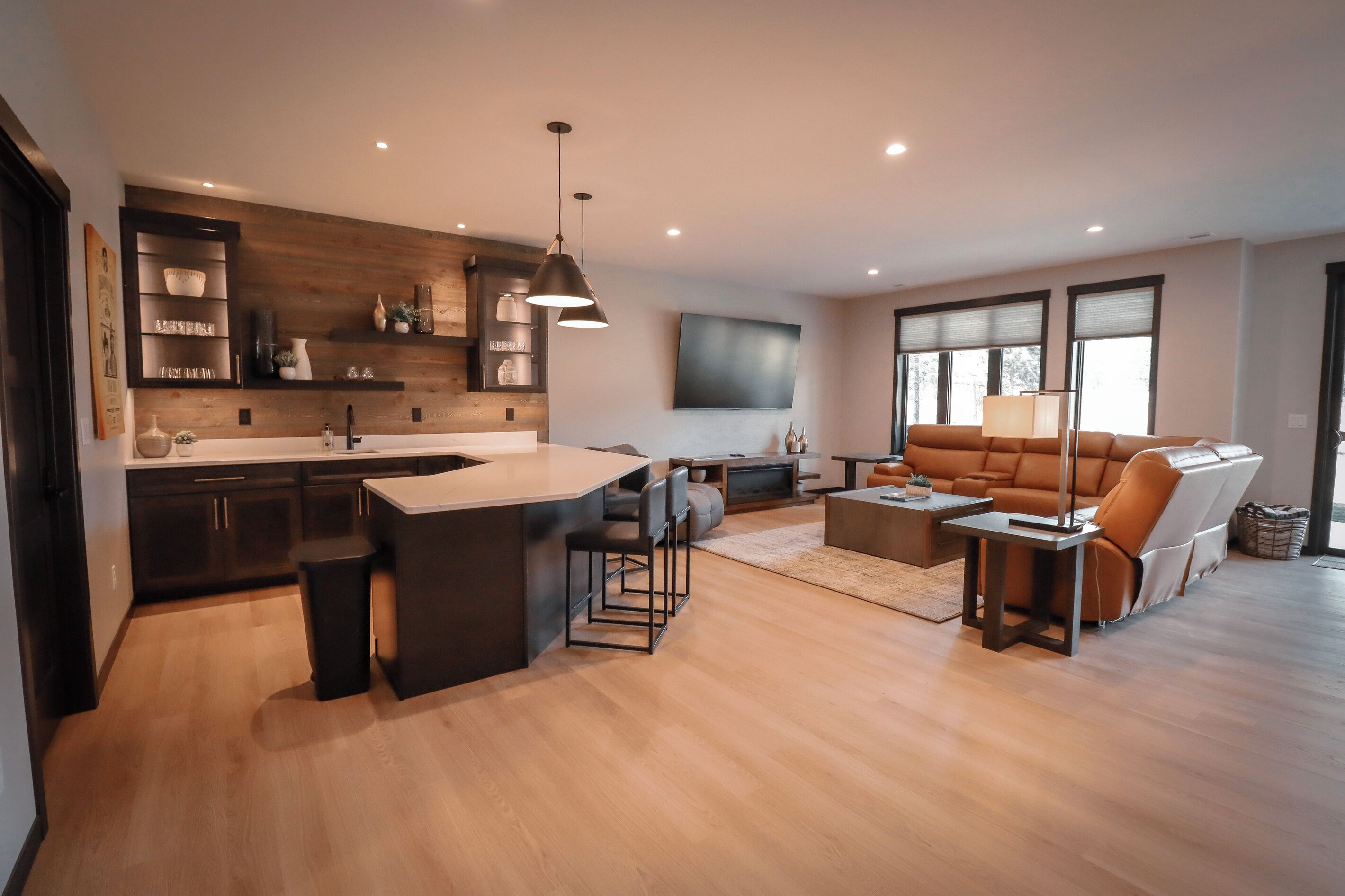 Una cocina moderna con una isla central, un comedor con sofá y mesa de centro, y una sala de estar con un ventanal grande.