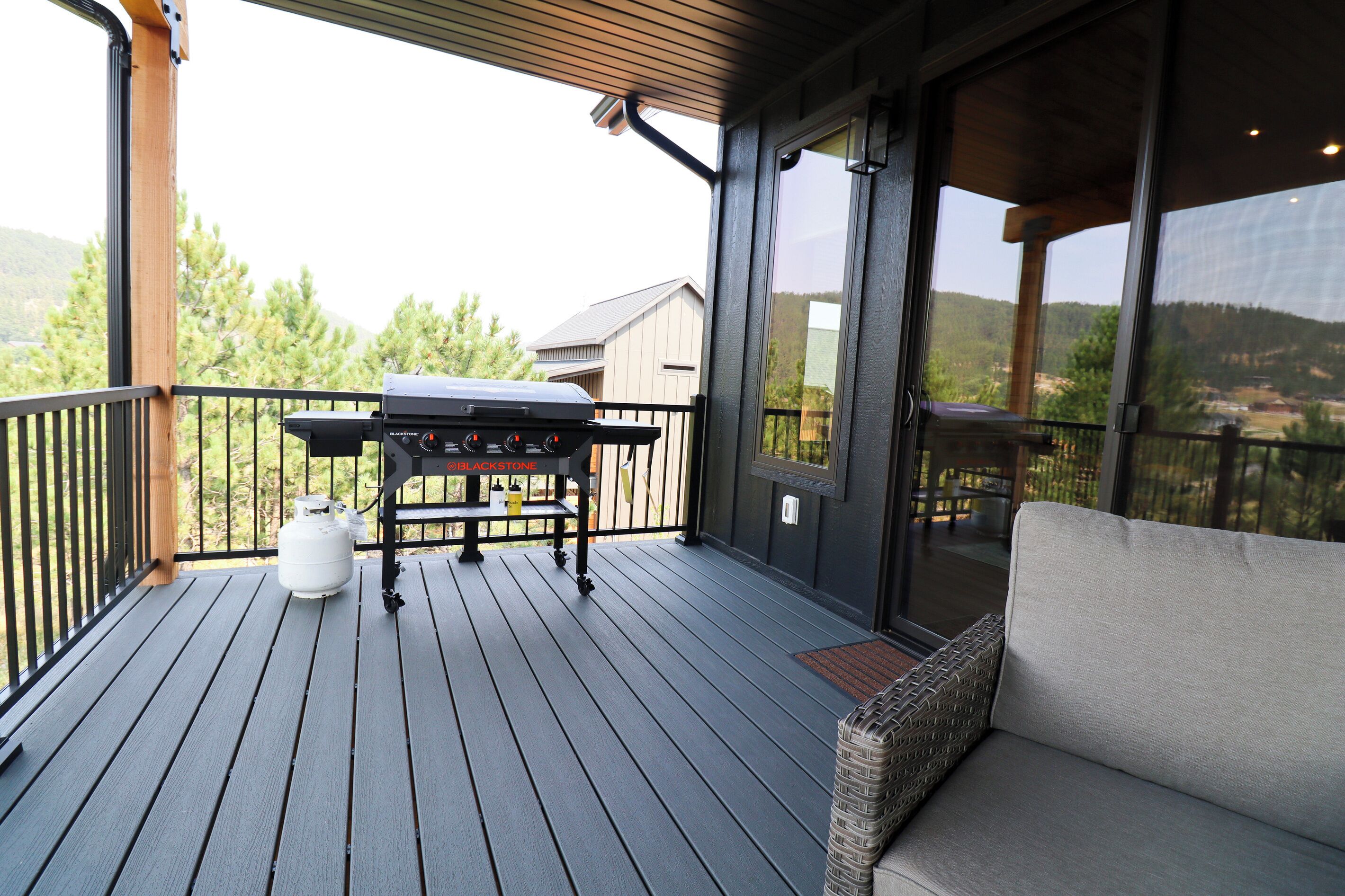 A wooden deck with a barbecue grill, a gas cylinder, and a wicker sofa.