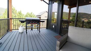 A wooden deck with a barbecue grill, a gas cylinder, and a wicker sofa.