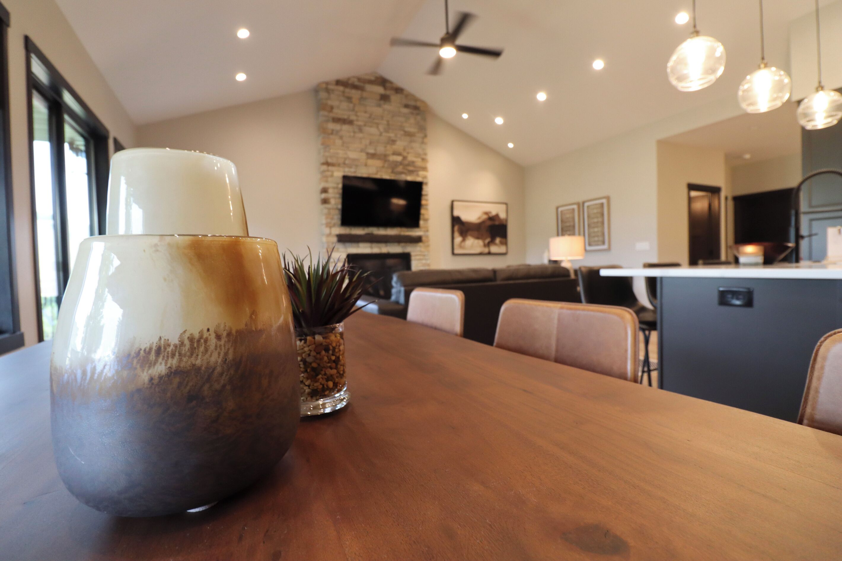A modern kitchen with a stone wall, a dining area with a wooden table, and a ceiling fan.