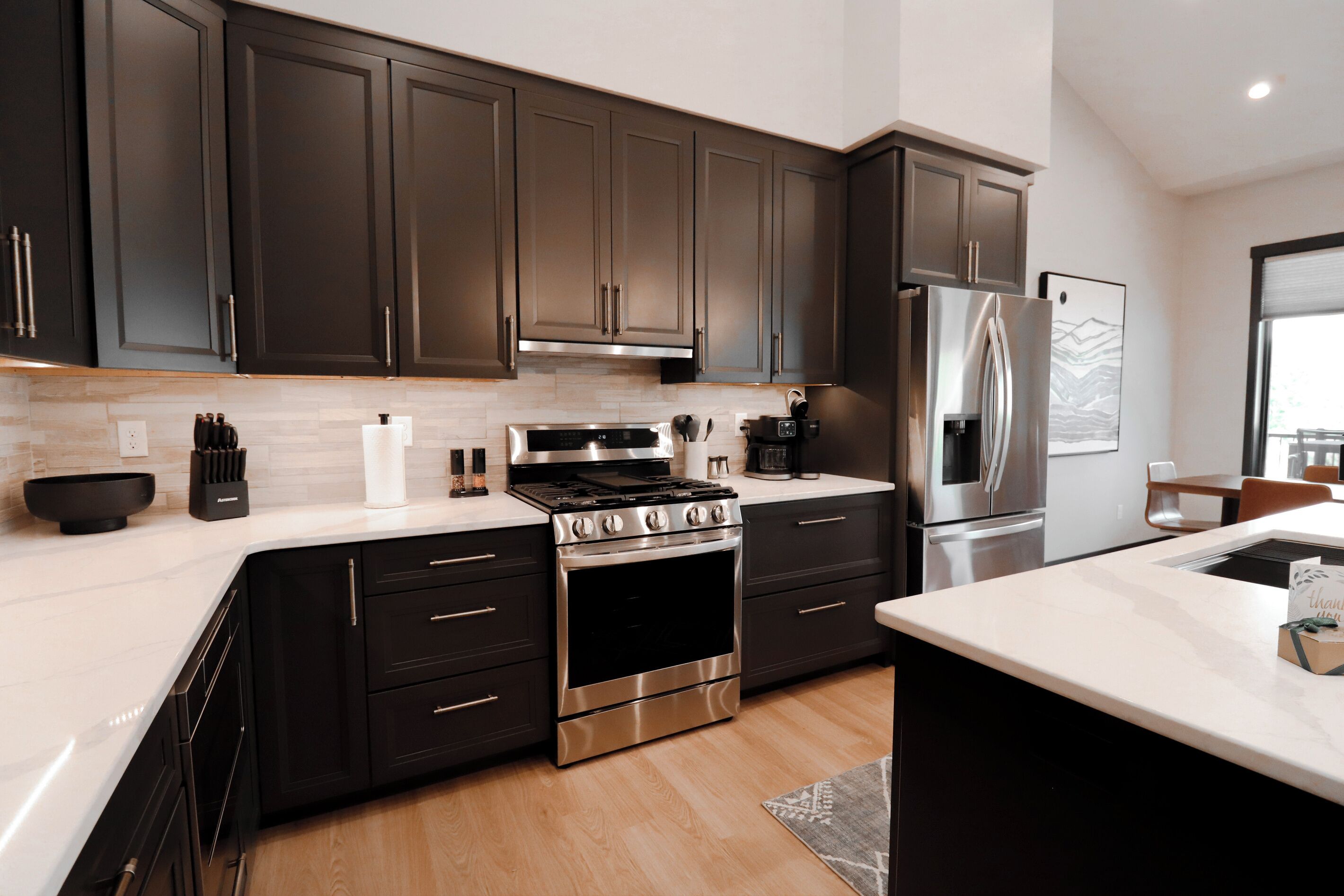 A modern kitchen with dark cabinets, stainless steel appliances, and a marble countertop.