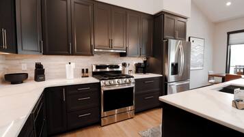 A modern kitchen with dark cabinets, stainless steel appliances, and a marble countertop.