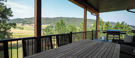 A wooden deck with a grill and outdoor furniture, overlooking a rural landscape with trees and hills.