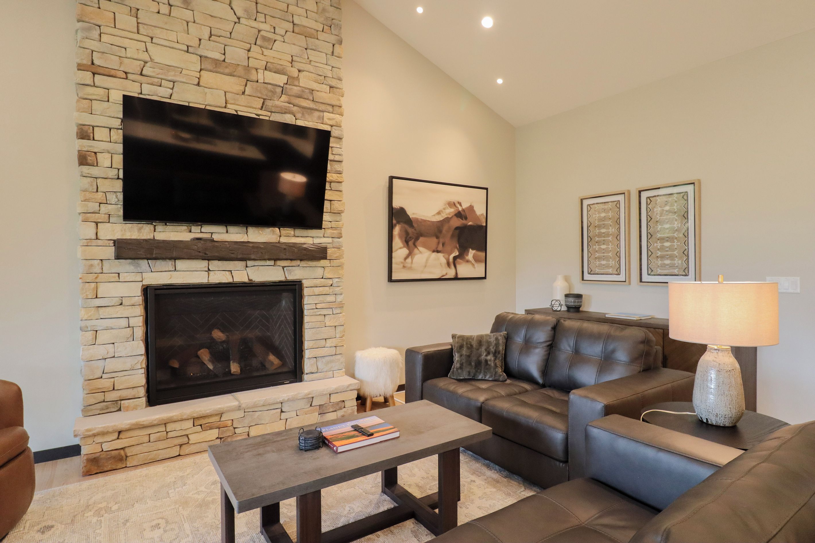 A living room with a stone fireplace, a leather sofa, a coffee table, and a mounted TV.