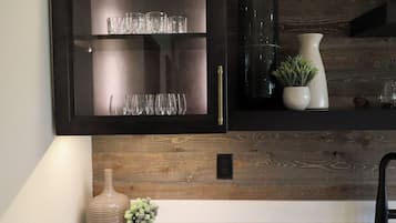 A kitchen with a dark wooden cabinet, a white countertop, and a rustic wooden wall.