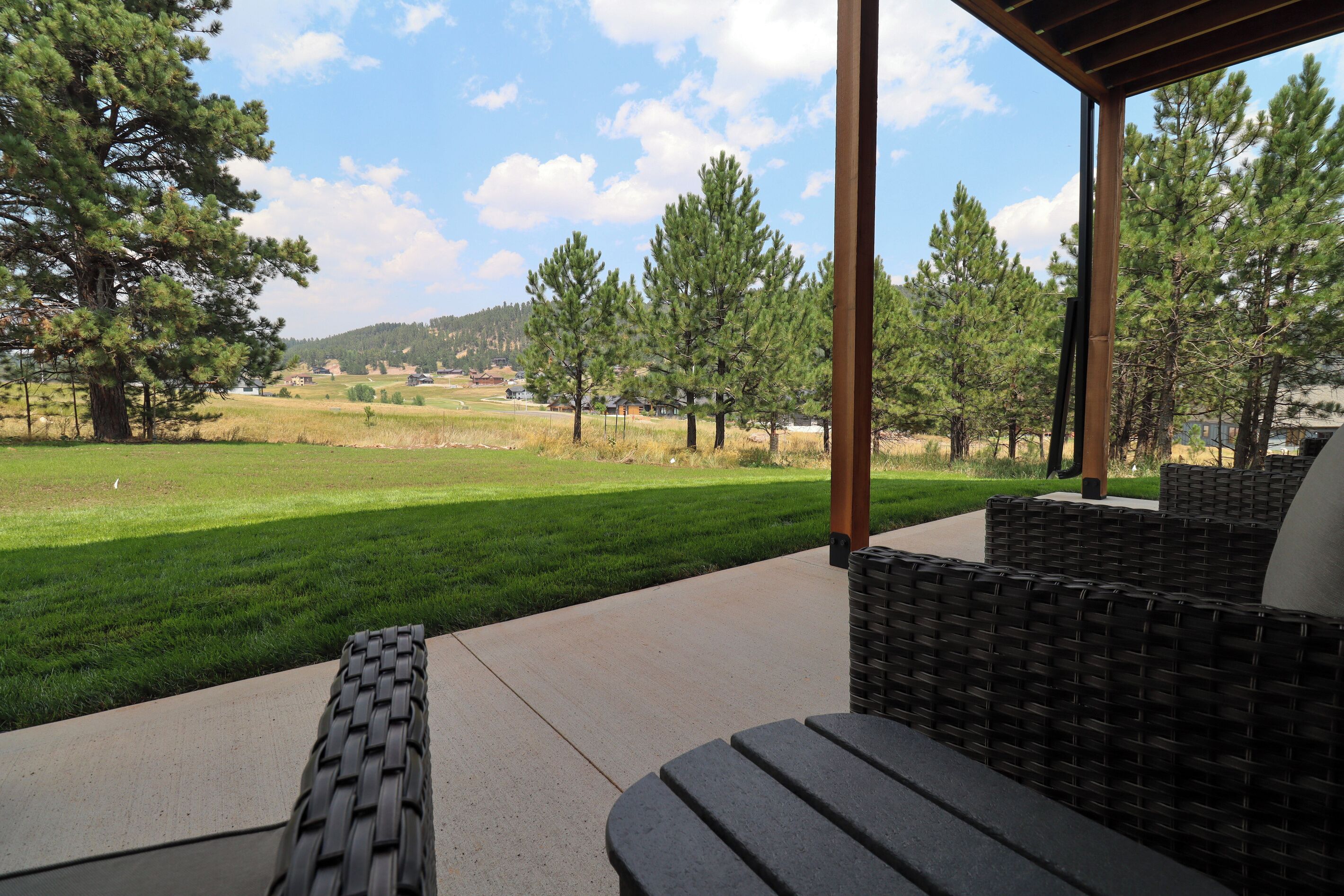 A covered outdoor seating area with a view of a grassy field and trees.