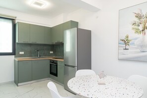 Una cocina moderna con armarios verdes, horno empotrado y una mesa redonda con sillas.