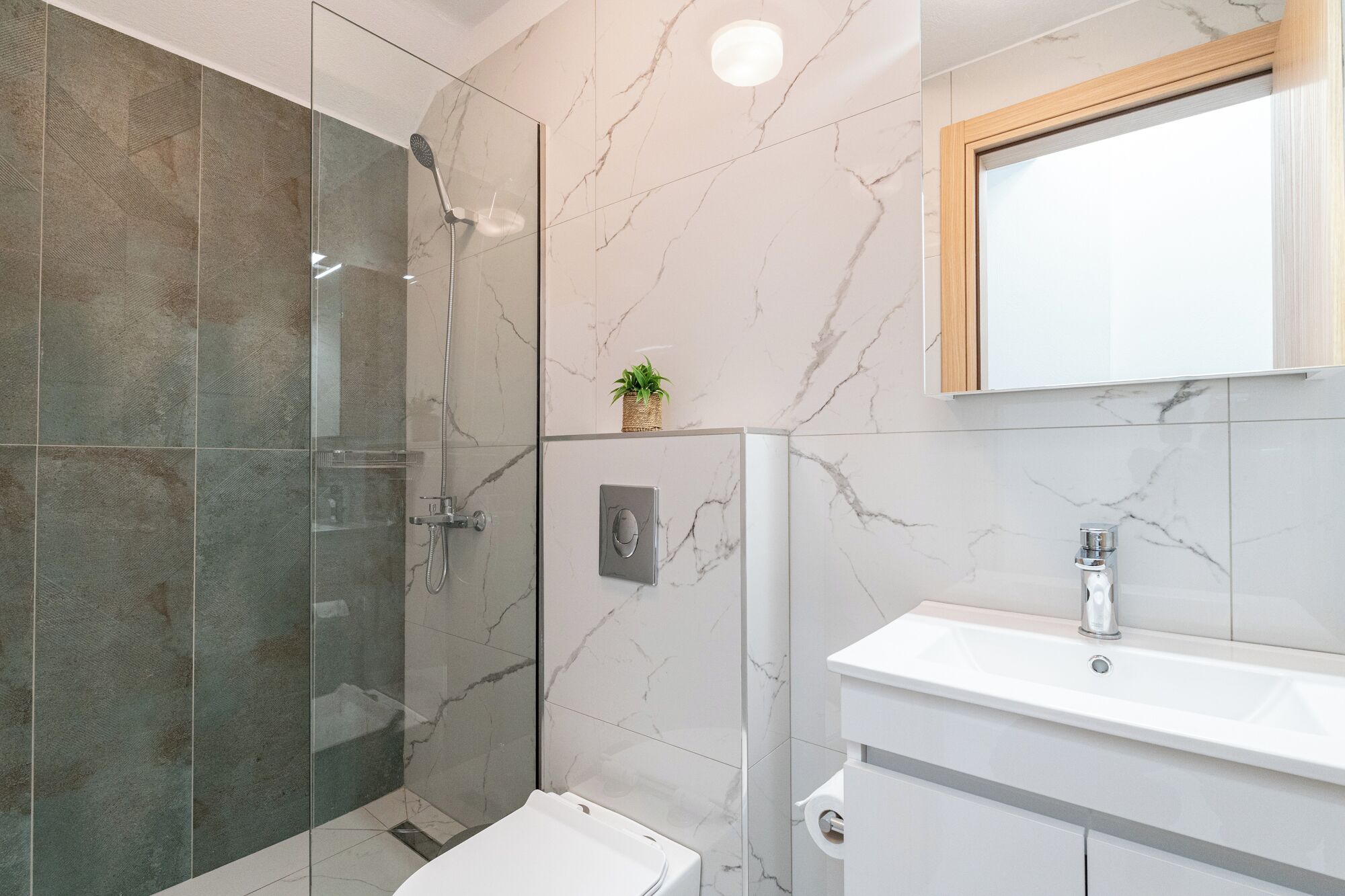 A bathroom with a glass shower enclosure, a white sink, and a marble-tiled wall.