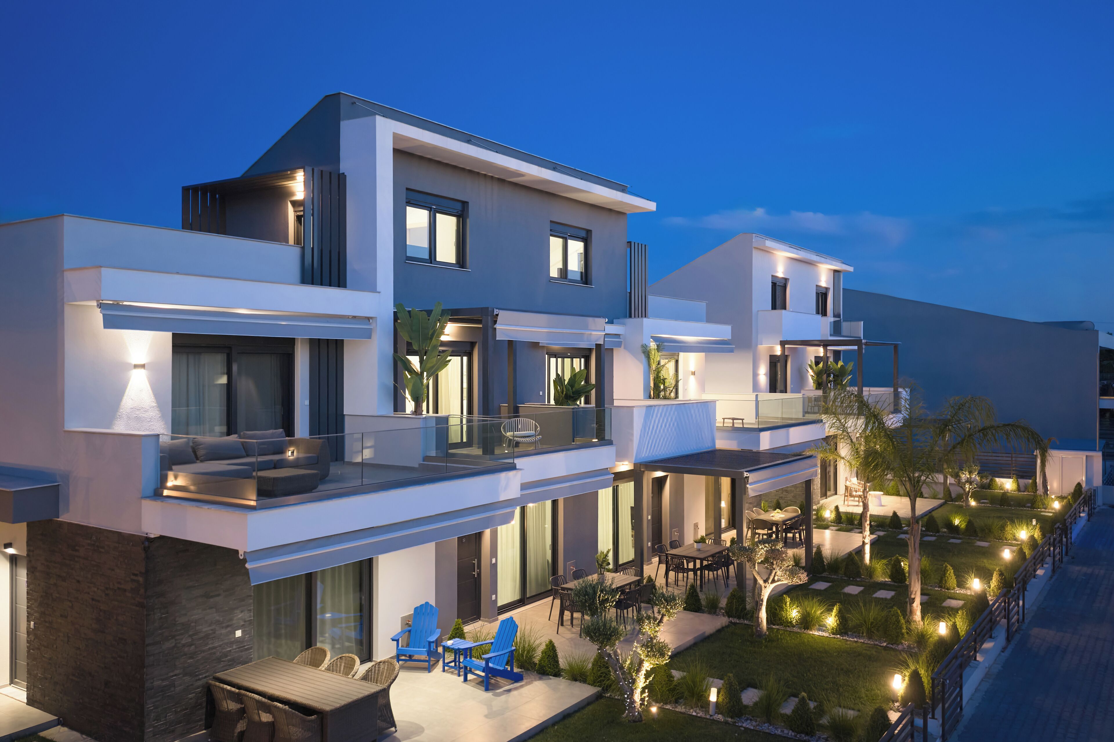 Un moderno edificio residencial de varios pisos con un balcón, zona de estar exterior y un jardín bien iluminado.