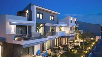 Un moderno edificio residencial de varios pisos con un balcón, zona de estar exterior y un jardín bien iluminado.