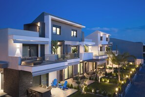 Un moderno edificio residencial de varios pisos con un balcón, zona de estar exterior y un jardín bien iluminado.