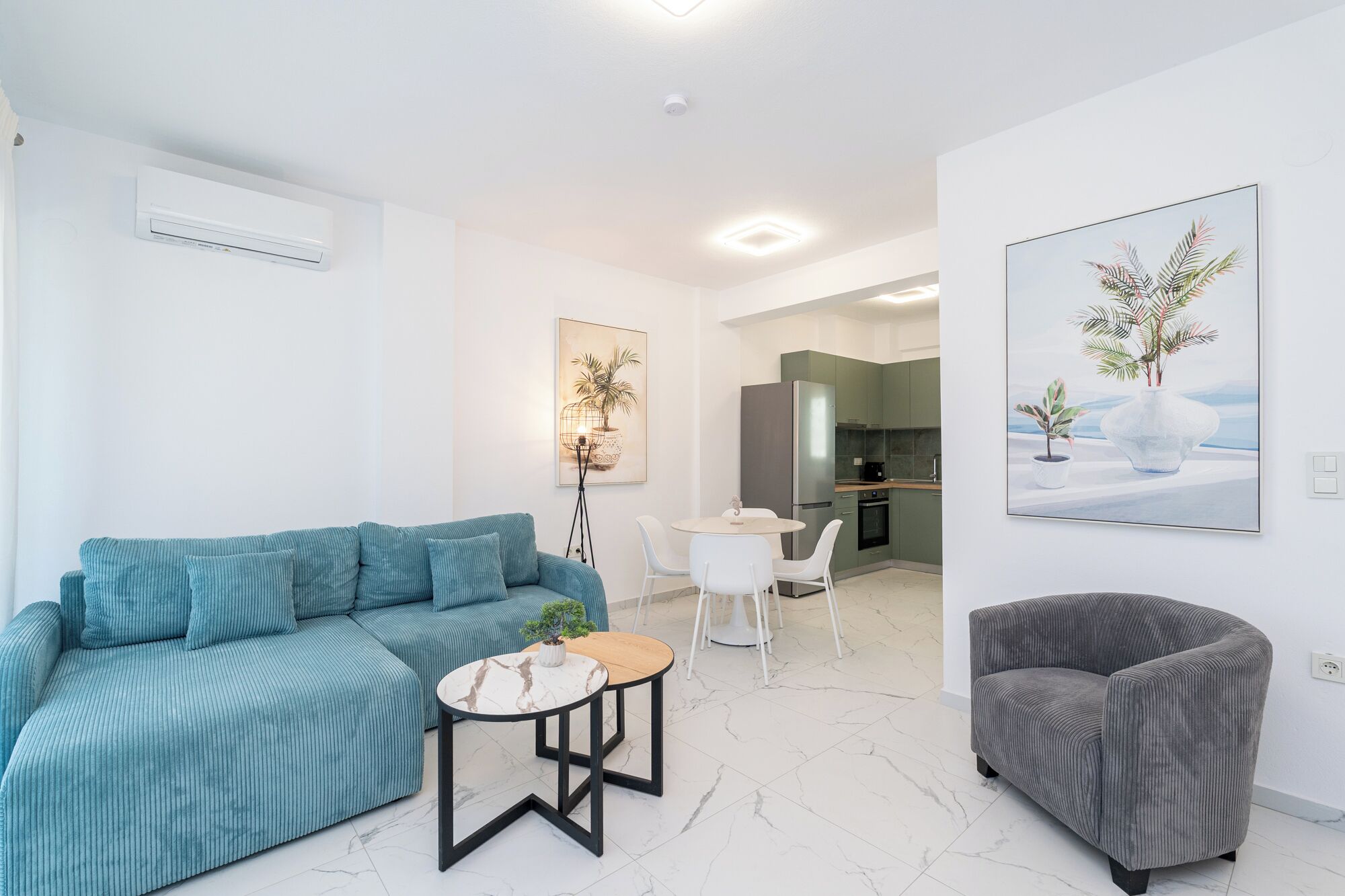 Una sala moderna con un sofá, una mesita redonda, un sillón gris y una cocina al fondo.