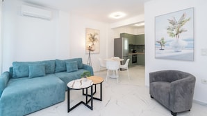 Un salon moderne avec un canapé, une petite table ronde, un fauteuil gris et une cuisine en arrière-plan.