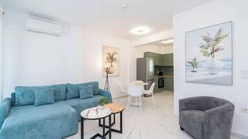 Una sala moderna con un sofá, una mesita redonda, un sillón gris y una cocina al fondo.