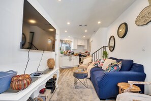 Ein Wohnzimmer mit einem blauen Sofa, einem Couchtisch, einem an der Wand befestigten Fernseher und einer Küche im Hintergrund.