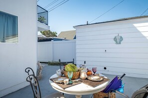A patio with a table set for a meal, a decorative shell sign, and a fenced backyard. - Chic 3-bedroom Modern Home Near SoFi Stadium & LAX, Comfortable with AC & WIFI (Inglewood)