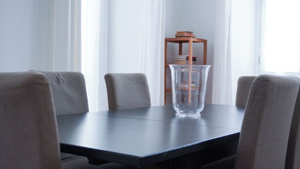 A dining table with four chairs, a clear glass vase, and a wooden side table with books. - Piazza Duomo Exclusive Family Apartment (Milano)