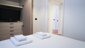 A hotel room with a bed, a TV on a cabinet, and a hallway leading to another room. - Piazza Duomo Exclusive Family Apartment (Milano)