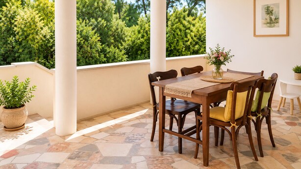Une terrasse couverte avec une table et des chaises en bois, un vase rempli de fleurs et un tableau encadré accroché au mur.