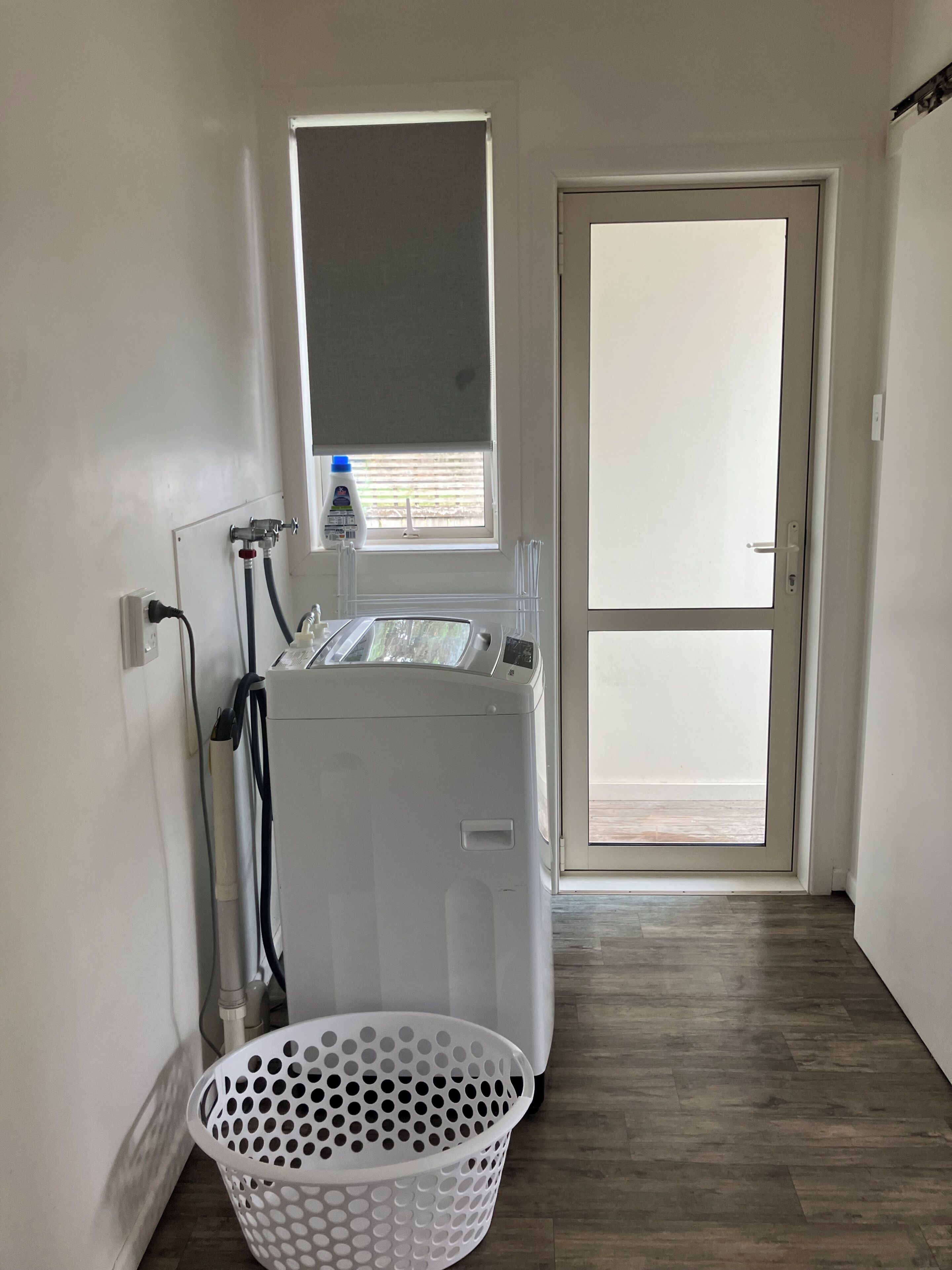 A laundry room with a washing machine, a dryer, a window with a blind, and a door leading to an outdoor area.