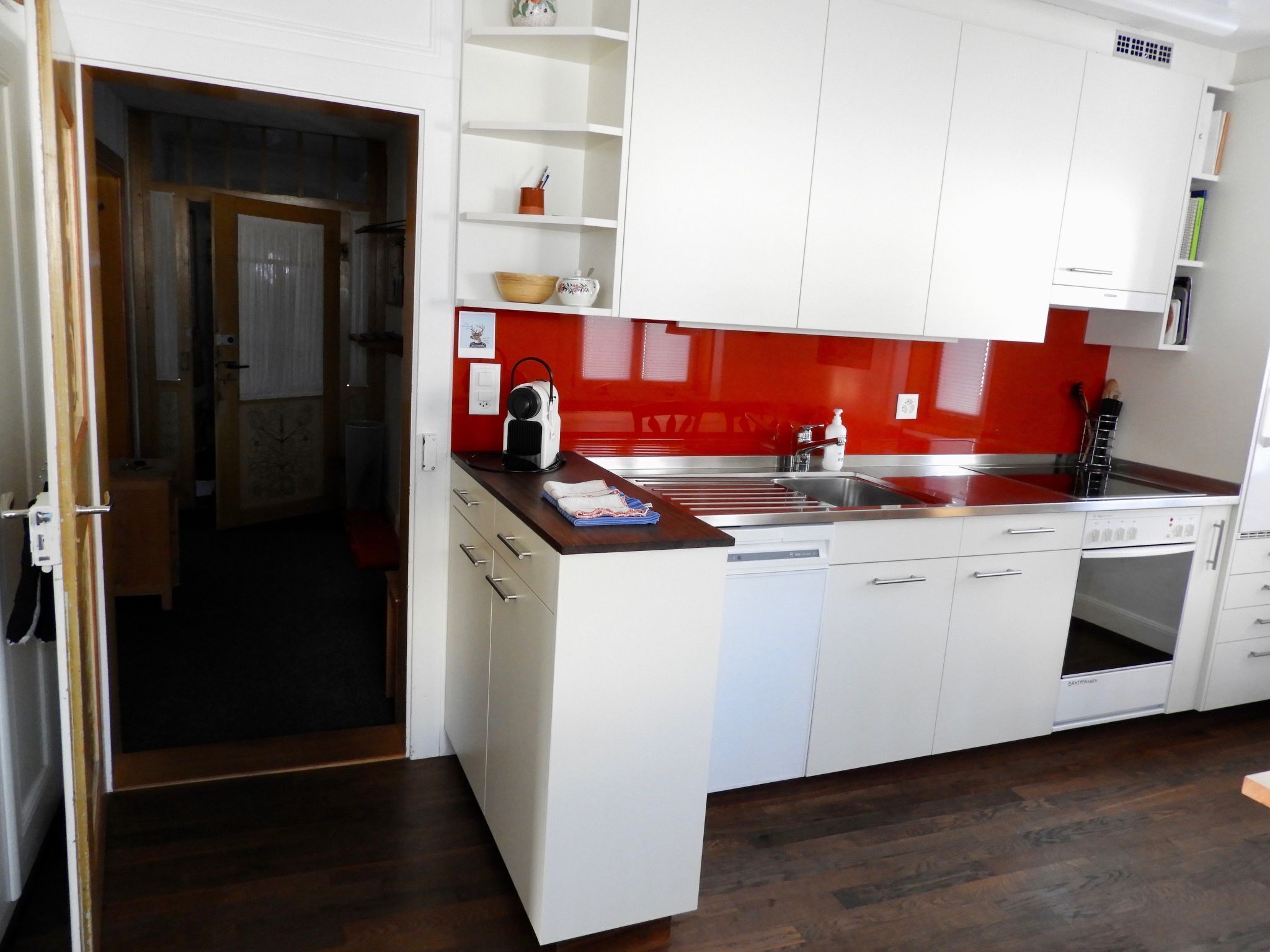 Cocina moderna con armarios blancos, salpicadero rojo y lavavajillas.