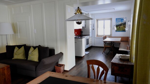 En stue med en sofa, et spisebord og et køkken i baggrunden.