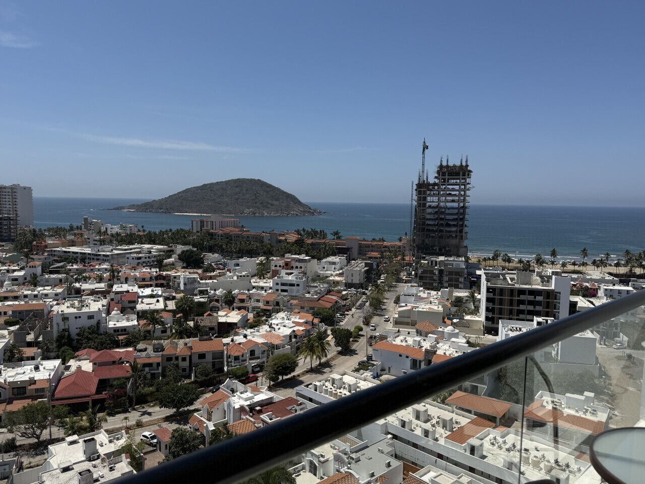 Eine Küstenstadtansicht mit einem markanten Gebäude im Bau, einer Erhebung im Hintergrund und freiem Blick auf das Meer.