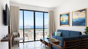 A modern living room with a sofa, a dining table, and chairs, a TV mounted on the wall, and a large window with a city view. - Accommodation with beautiful views, with a pool. (Mazatlán)