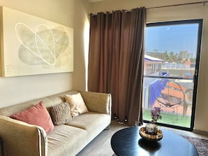 Ein Wohnzimmer mit einer Couch, einem Couchtisch und Blick auf einen Balkon mit Gartenmöbeln.