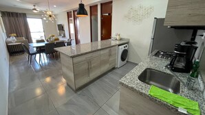 A modern kitchen with a central island, a built-in washing machine, and a dining area with a table and chairs. - Steps from the beach in the Golden Zone (Mazatlán)