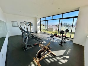 Ein Fitnessstudio mit Cardiogeräten, Krafttrainingsgeräten und großen Fenstern mit Blick auf die Stadt.