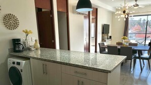 Eine moderne Küche mit integriertem Waschmaschine, einem Essbereich mit Tisch und Stühlen sowie einem Blick ins Freie durch ein großes Fenster.